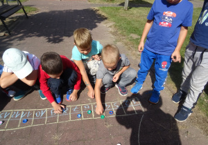 dzieci bawią się w wyścigi kapselkami, mają narysowany start z miejscami startowymi kredą na chodniku